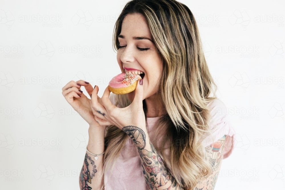 Blonde girl in a pink t shirt biting into a pink iced donut : Austockphoto Blonde girl in a pink t shirt biting into a pink iced donut - Australian Stock Image