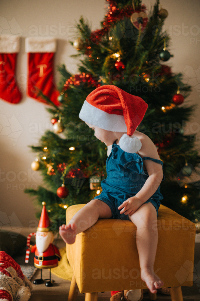 blonde girl sits on a yellow stool by a Christmas tree - Australian Stock Image