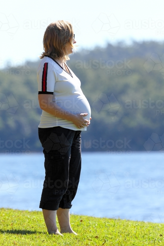 Blonde lady in mid-thirties caressing her pregnant belly. - Australian Stock Image