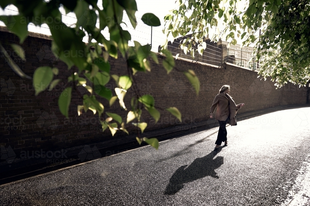 Blonde lady walking down a backlit street / alley looking back - Australian Stock Image