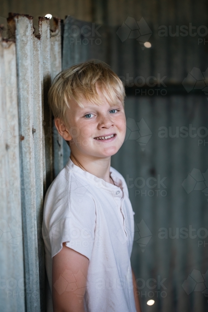 Blonde pre-teen boy with relaxed pose sitting in rustic outdoor county setting - Australian Stock Image