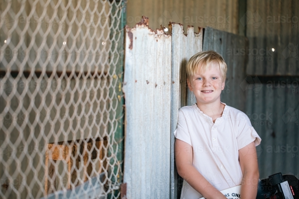 Blonde pre-teen boy with relaxed pose sitting in rustic outdoor county setting - Australian Stock Image