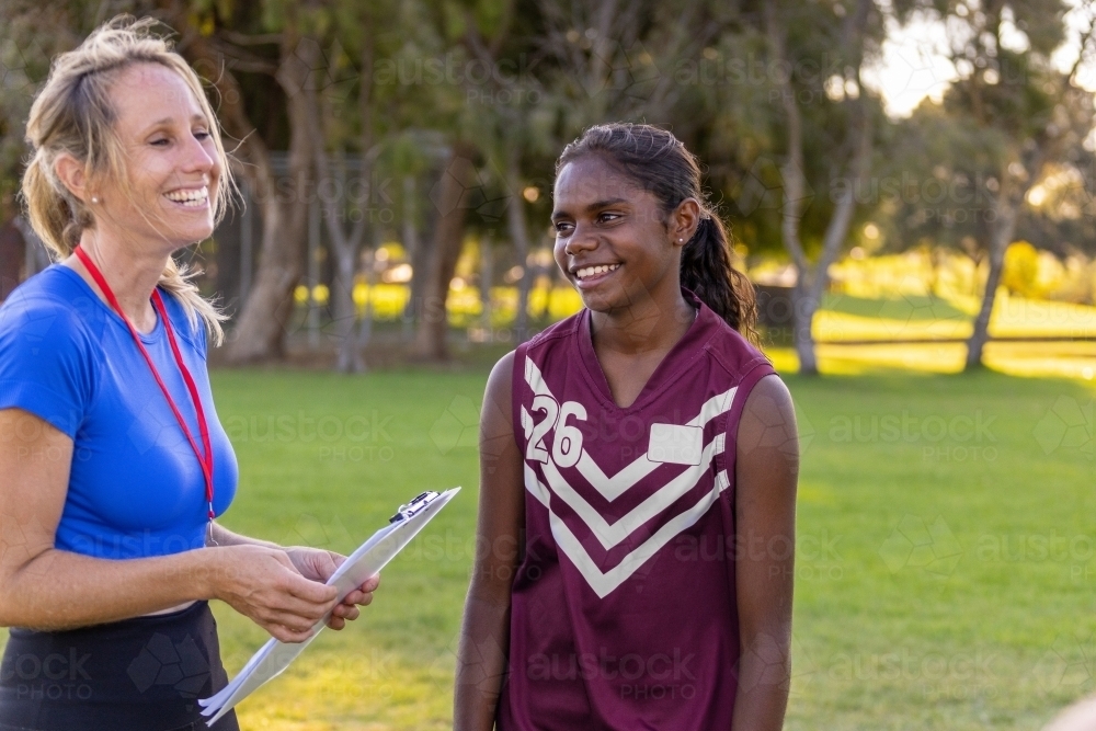 blonde woman holding clipboard coaching aboriginal football player - Australian Stock Image