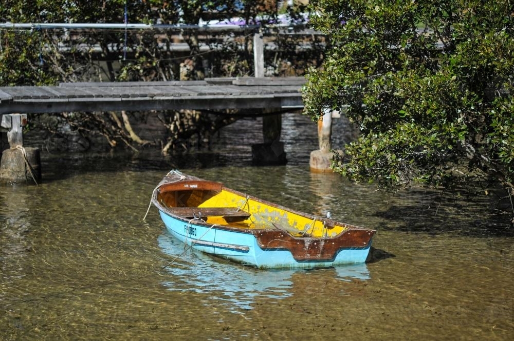 Blue boat in shallow water with wooden bridge - Australian Stock Image