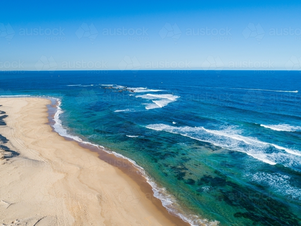Blue green waves in vast ocean washing up to beach in sunlight - Australian Stock Image