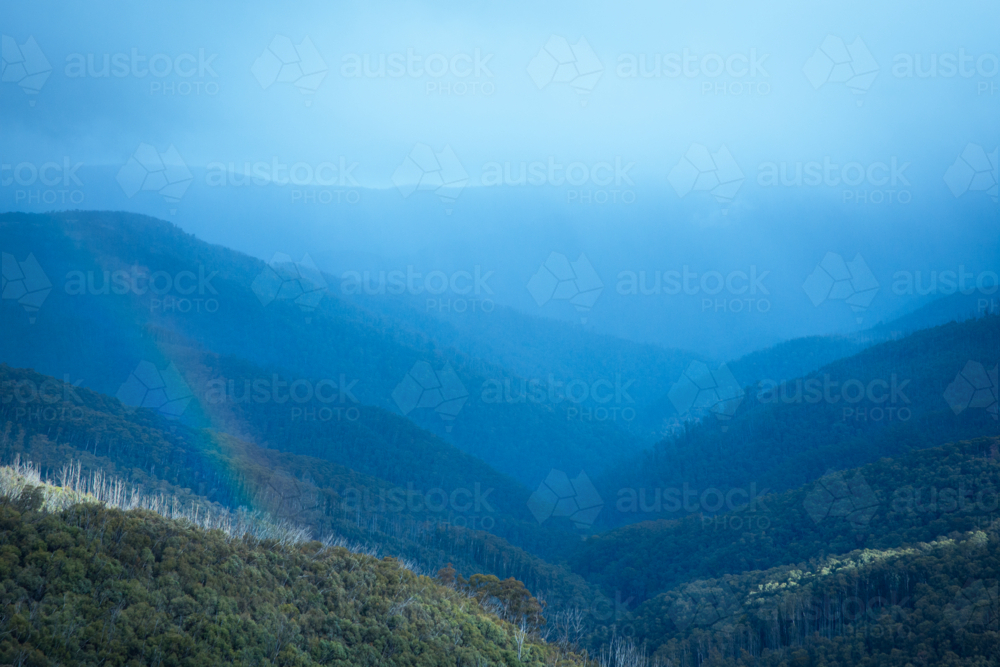 Blue hazy clouds and rainbow over mountain range at Mt Hotham - Australian Stock Image