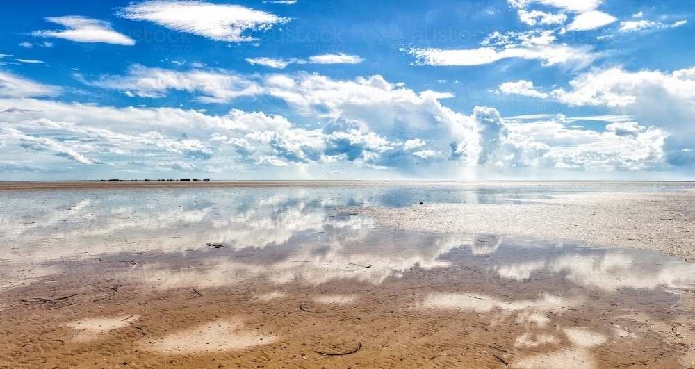 blue sky with clouds reflected in shallow water at beach - Australian Stock Image