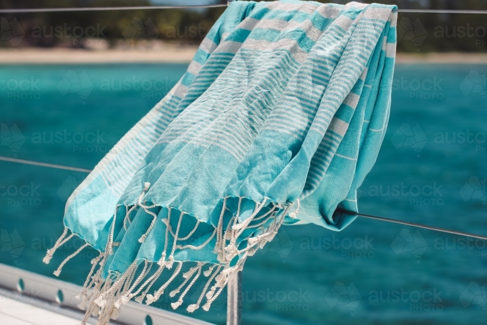 Blue turkish towel blowing on wire railing of boat on the water - Australian Stock Image