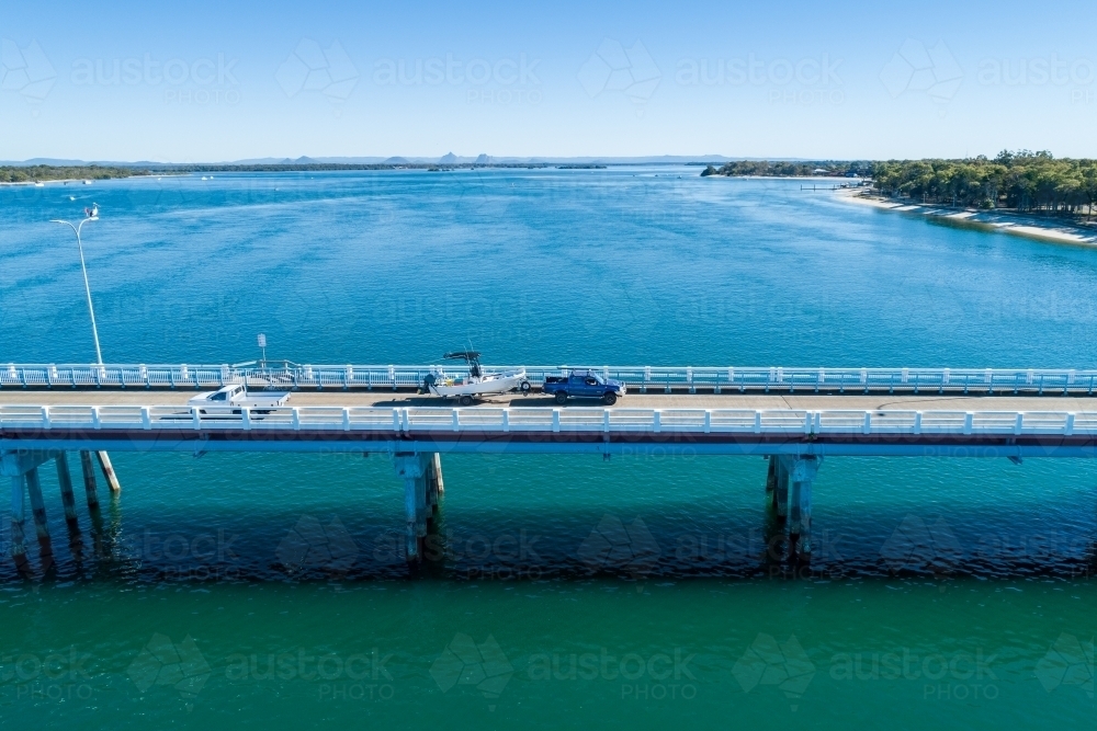 Blue ute towing a fishing boat on bridge over water. - Australian Stock Image