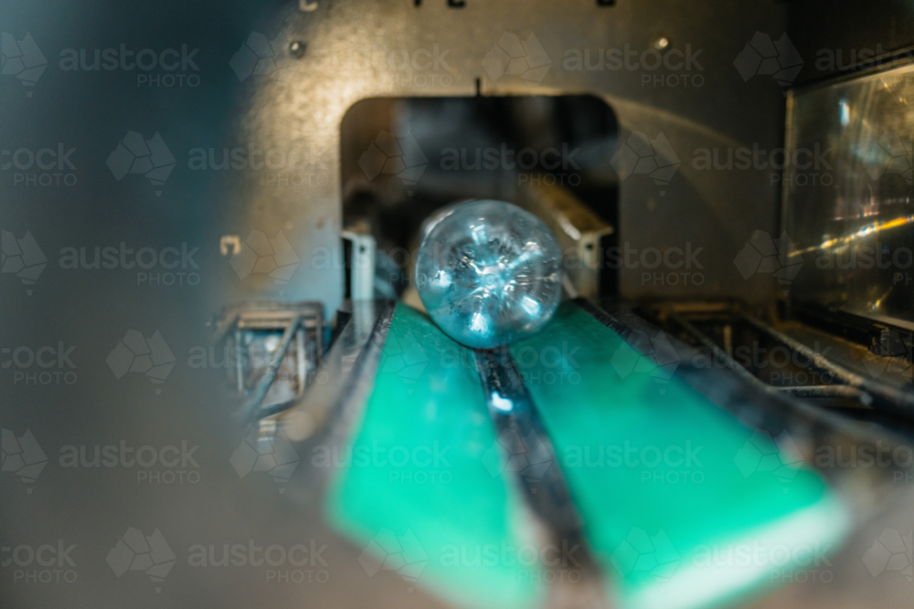 blur of plastic bottle moving on a green conveyor belt inside industrial recycling machinery - Australian Stock Image