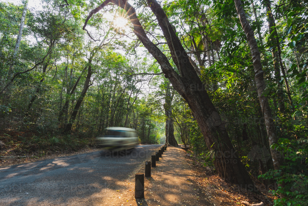 Blurred car driving on road through lush rainforest with sun star in Australia - Australian Stock Image