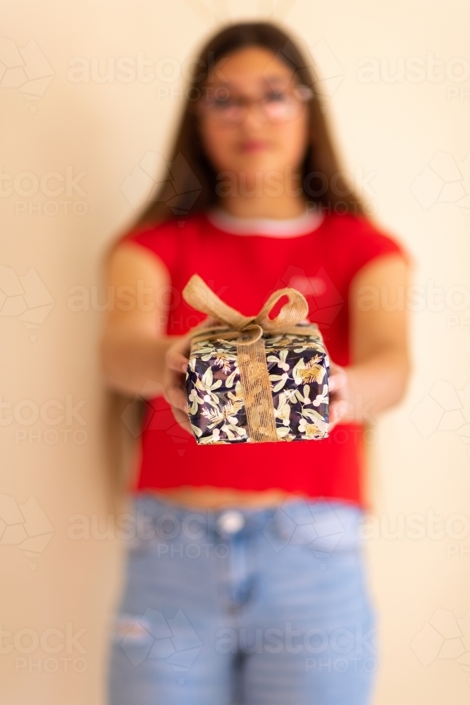 blurred girl in background with focus on gift being offered - Australian Stock Image