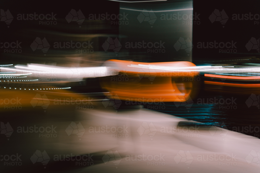 Blurred orange motion streaks glowing across dimly lit urban nightscape - Australian Stock Image