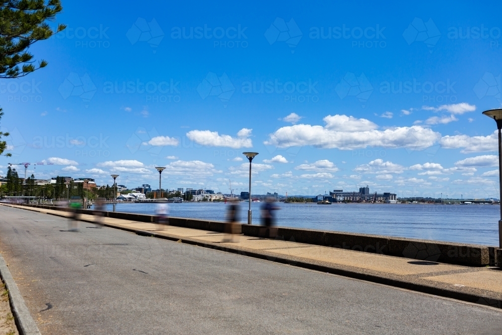 Blurred people walking and running along the foreshore footpath in Newcastle at midday - Australian Stock Image