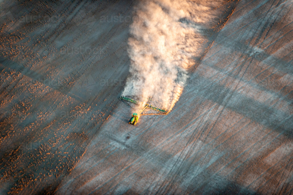 blurred tractor trailing dust across a dry paddock in early morning light, viewed from above - Australian Stock Image
