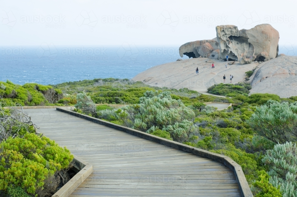 Boardwalk through brush to large rock formation by the ocean - Australian Stock Image