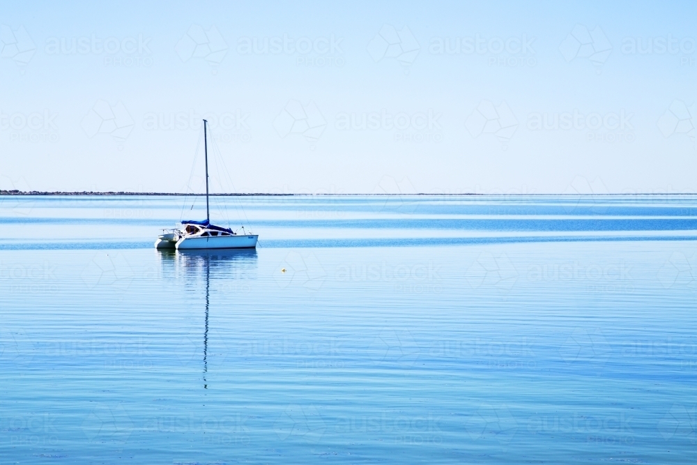 Boat anchored in calm bay with blue water and clear sky - Australian Stock Image