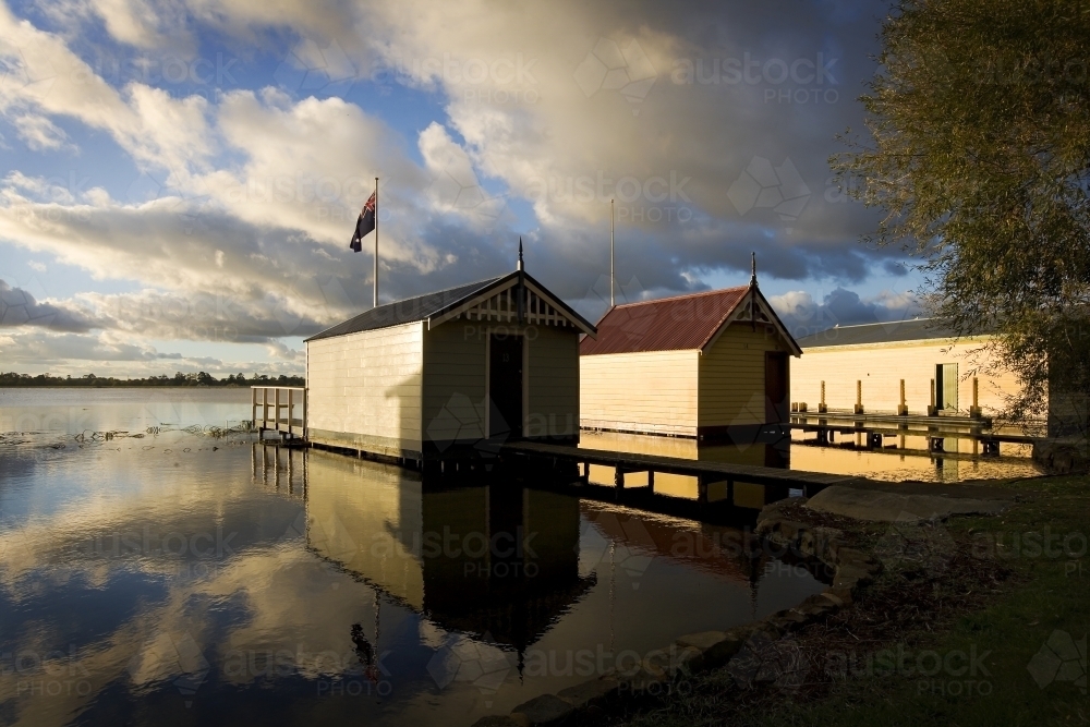 Boat sheds reflected in lake with dramatic sky - Australian Stock Image