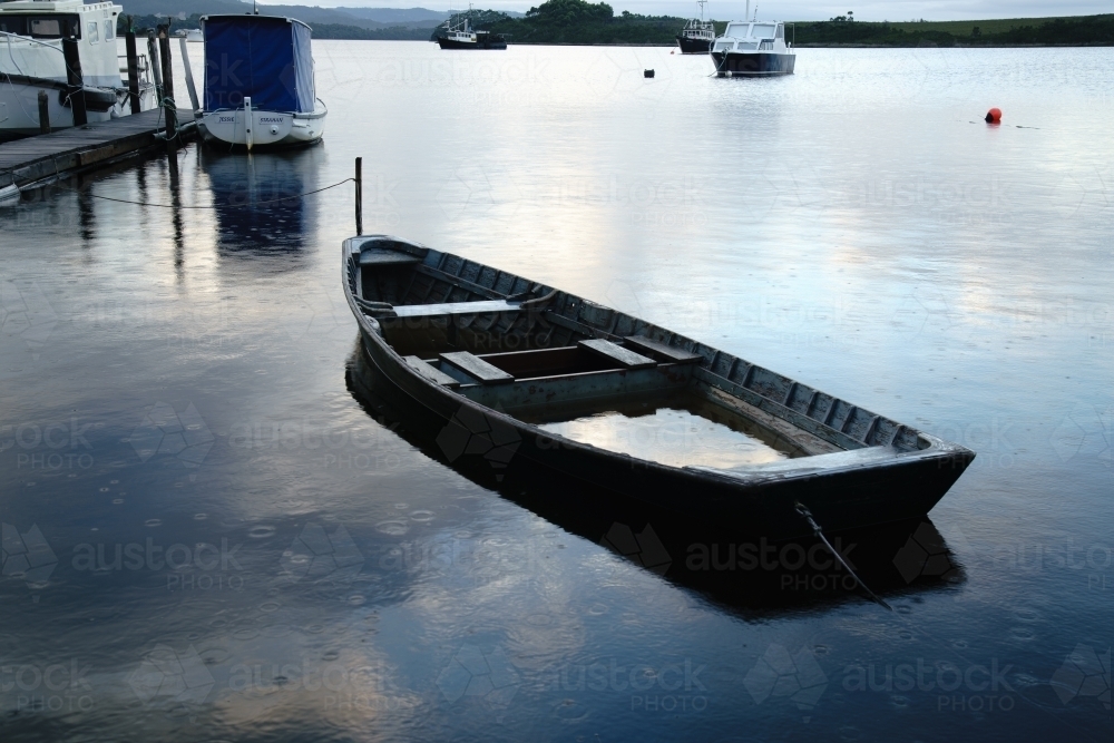 Boat with water in it moored in Morse Bay, Strahan, Tasmania - Australian Stock Image