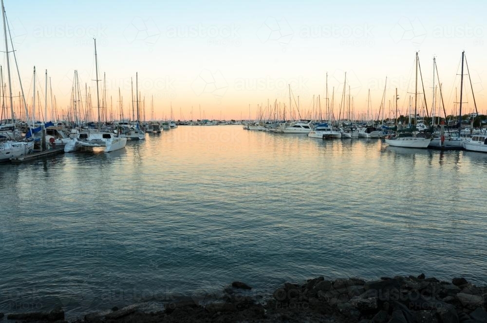 Boats and yachts moored either side of a channel in a marina in the early evening light - Australian Stock Image