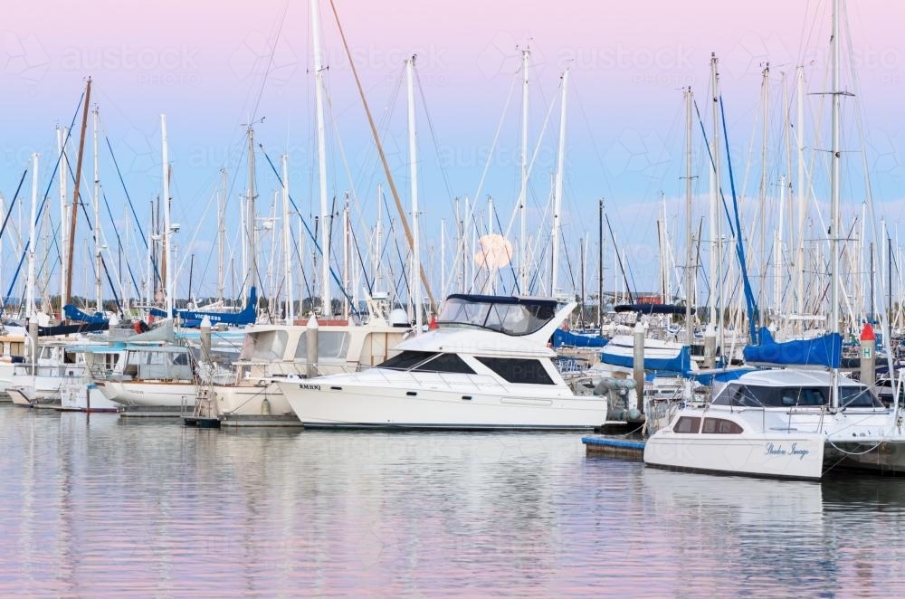 Boats and yachts moored with the moon rising in the sunset colours - Australian Stock Image