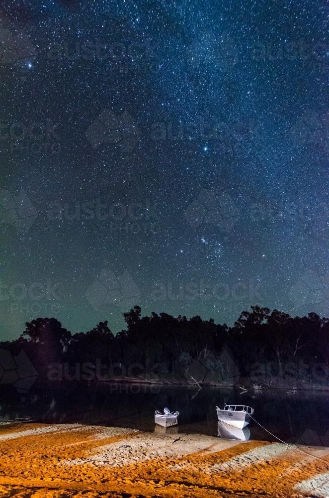 Boats moored on a riverbank with starry night sky - Australian Stock Image