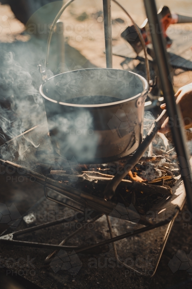 Boiling water in a pot over a campfire in the morning sun - Australian Stock Image