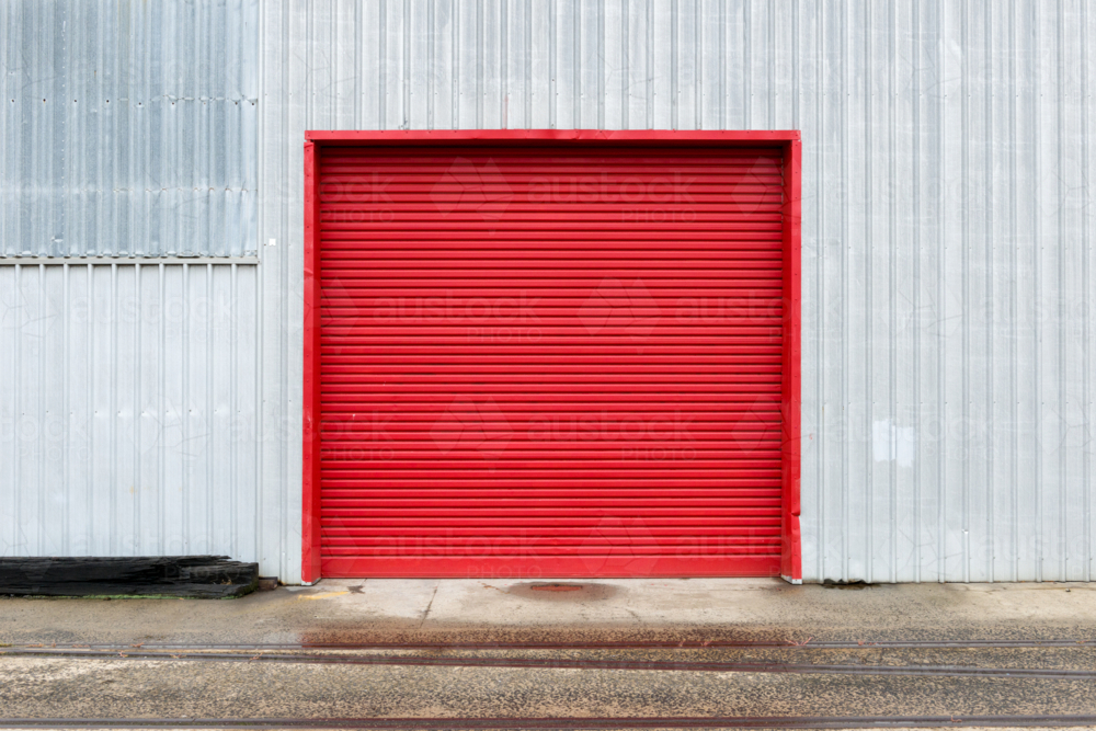 Bold red roller door on corrugated metal warehouse wall. - Australian Stock Image