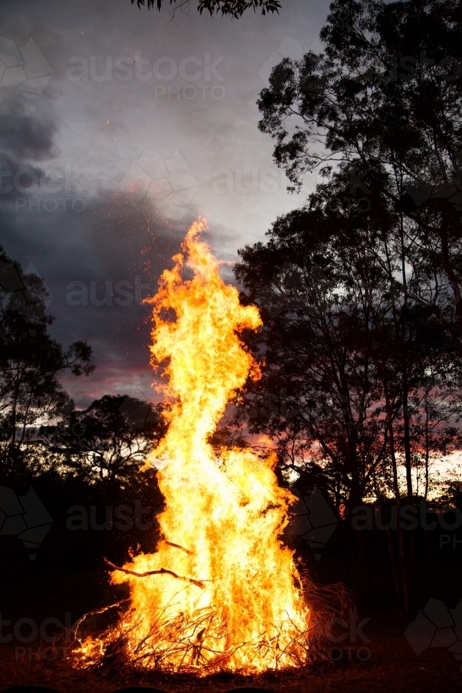 Bonfire burning high and bright in a paddock at sunset - Australian Stock Image