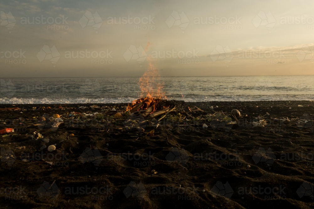 Bonfire burning on the dark sand at the beach at sunset - Australian Stock Image