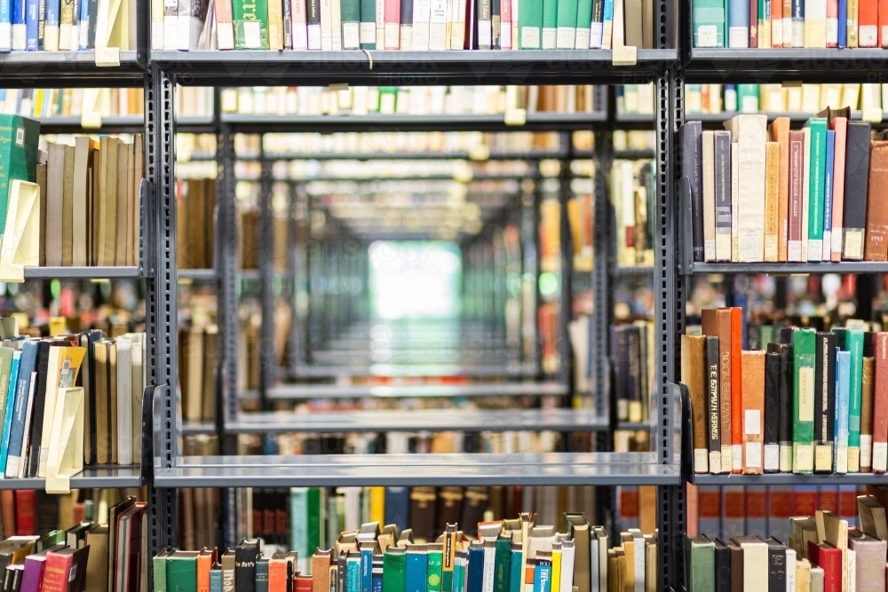 Books in rows on library shelves and window light through shelving - Australian Stock Image