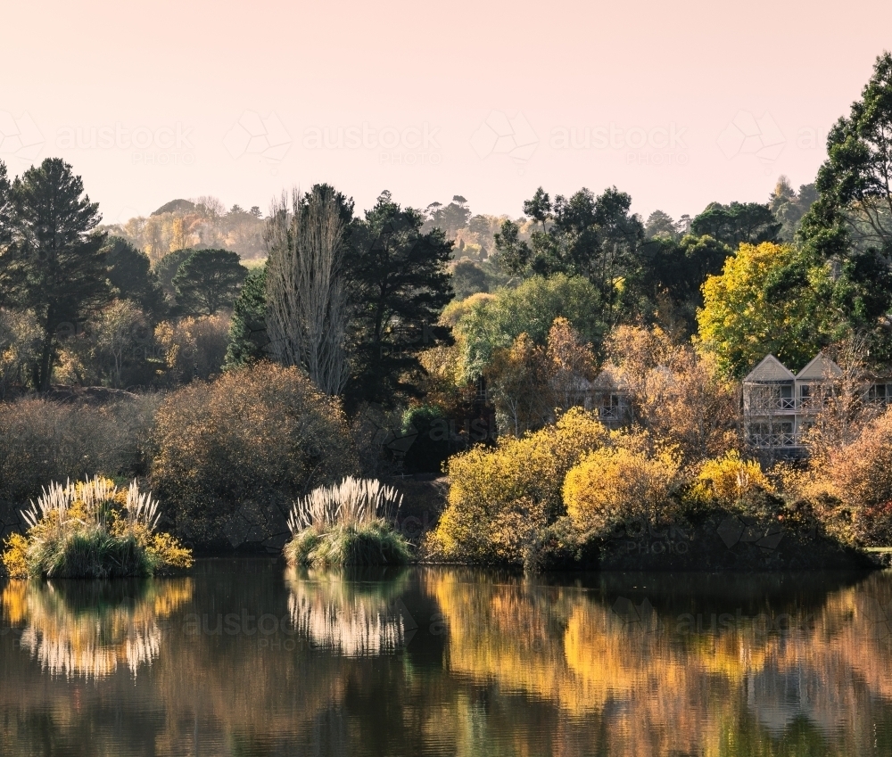 Boutique hotel by the lake, surrounded in lush green, yellow and brown trees, with water reflections - Australian Stock Image