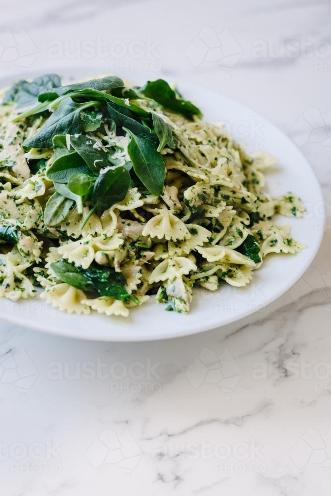 Image of bow tie pasta with pesto and spinach leaves Austockphoto