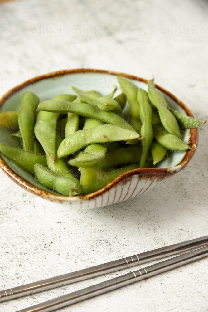 Image of bowl of edamame with metal chopsticks Austockphoto