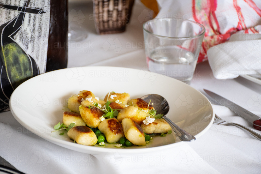 Bowl of Gnocchi with serving spoon on a dinner table - Australian Stock Image