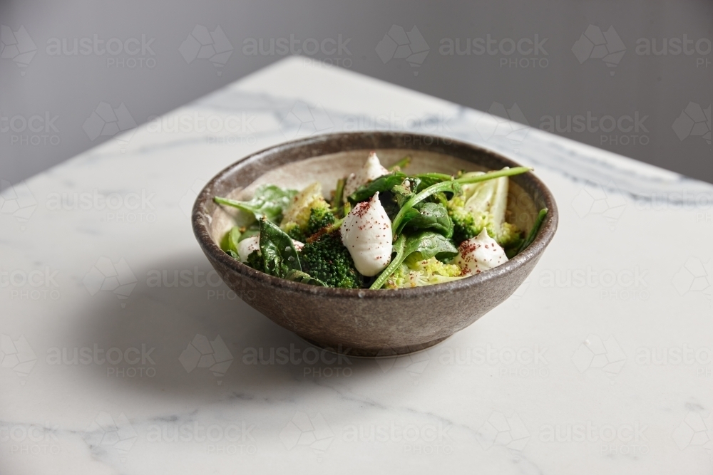 Bowl of greens, broccoli and burrata cheese on a table - Australian Stock Image