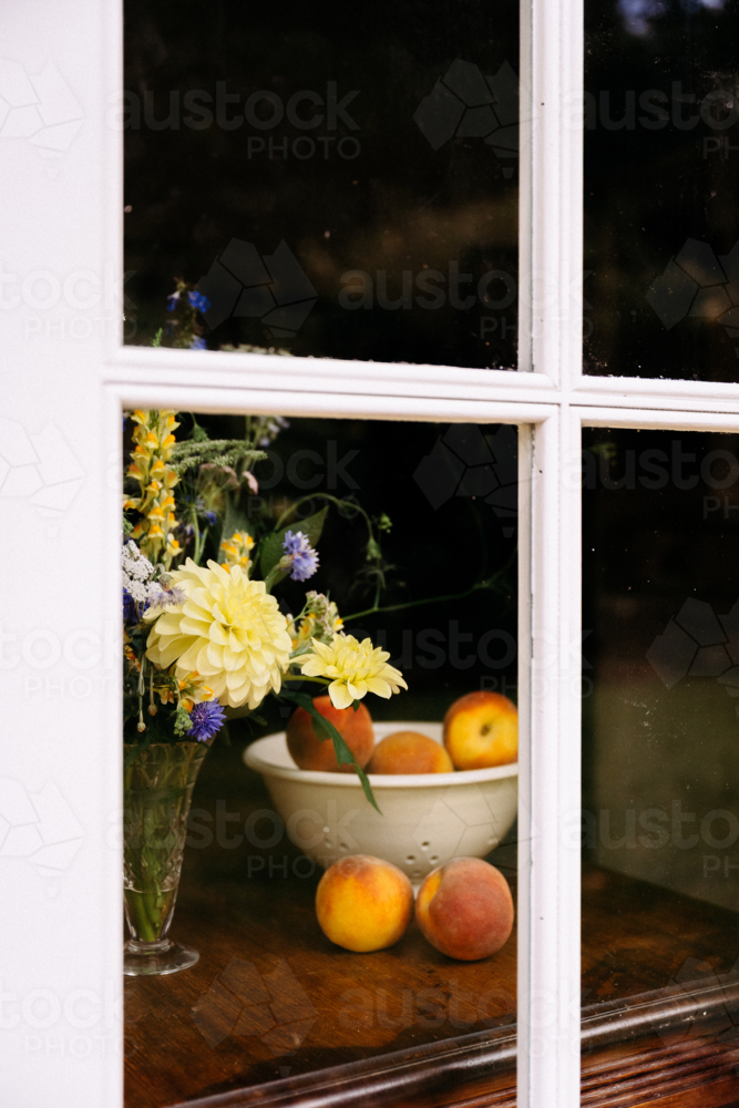 bowl of peaches and some flowers through a door - Australian Stock Image