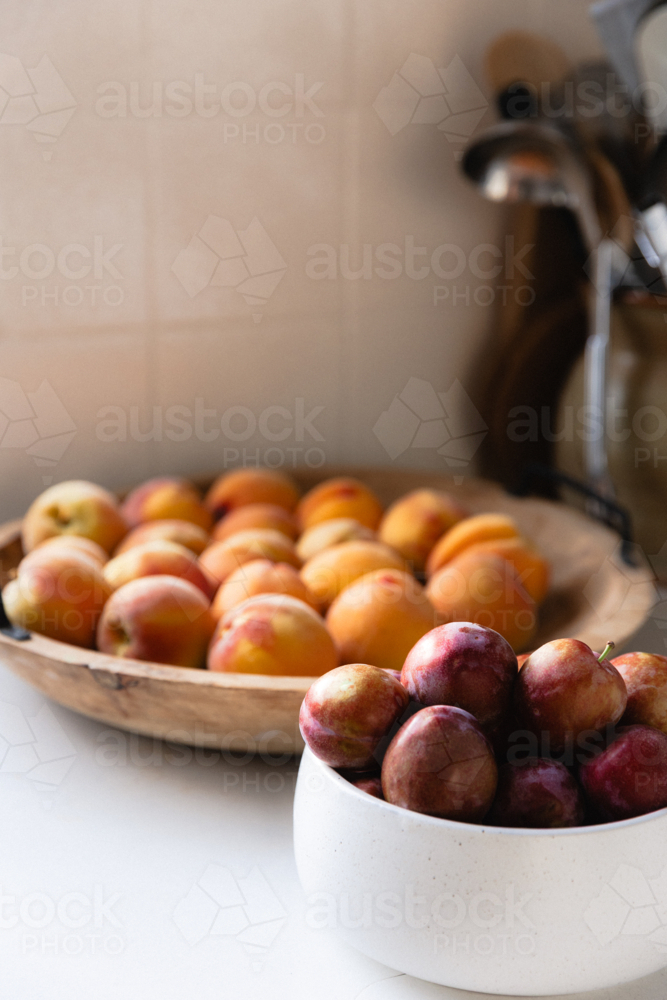 Bowls of freshly picked stone fruit on white kitchen bench - Australian Stock Image
