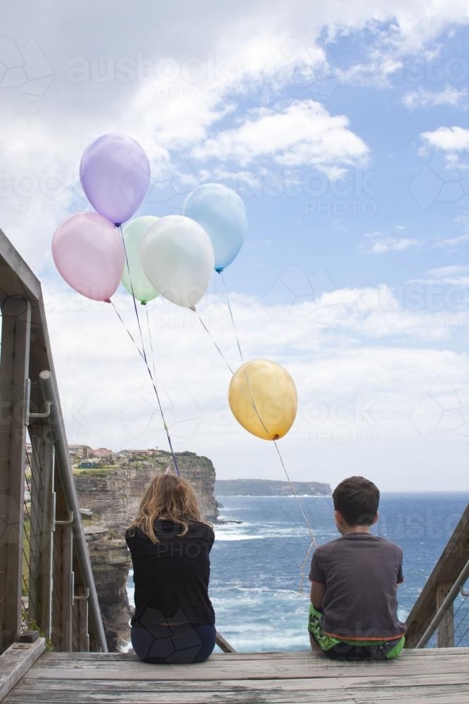 Boy and girl holding bunch of balloons at an ocean lookout - Australian Stock Image
