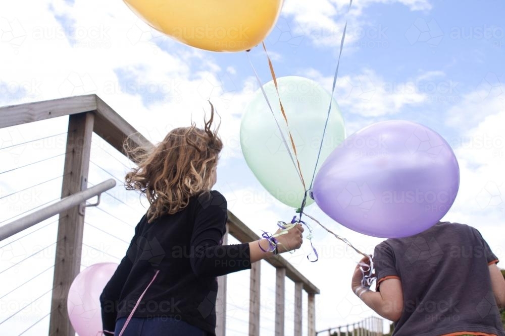 Boy and girl looking away into the wind holding balloons - Australian Stock Image