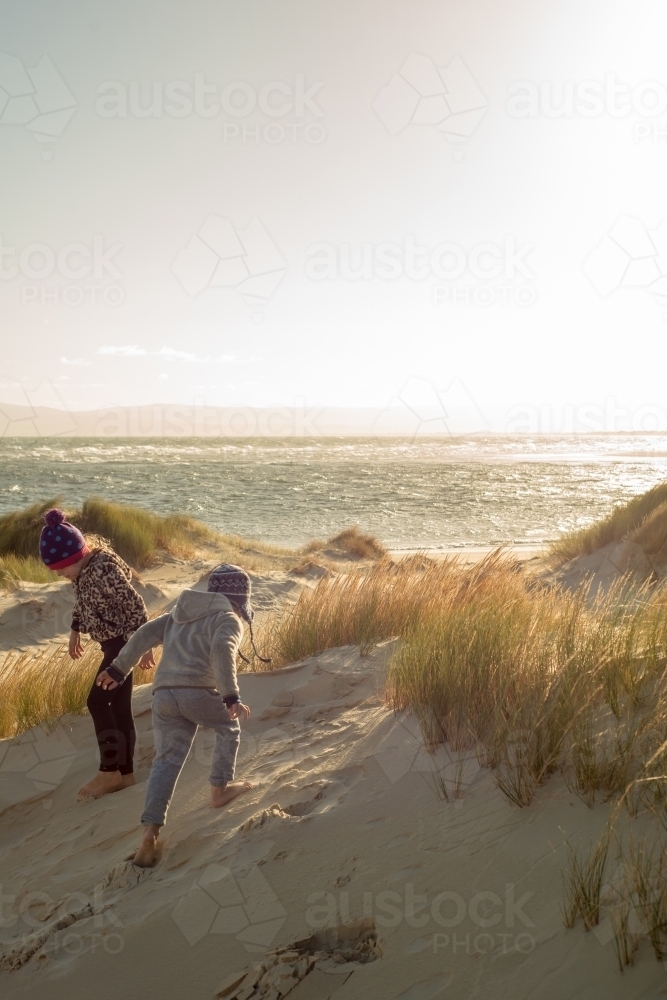 Boy and girl playing on sand dunes at sunset - Australian Stock Image