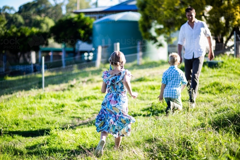 Boy and girl run to their dad through farm paddock - Australian Stock Image