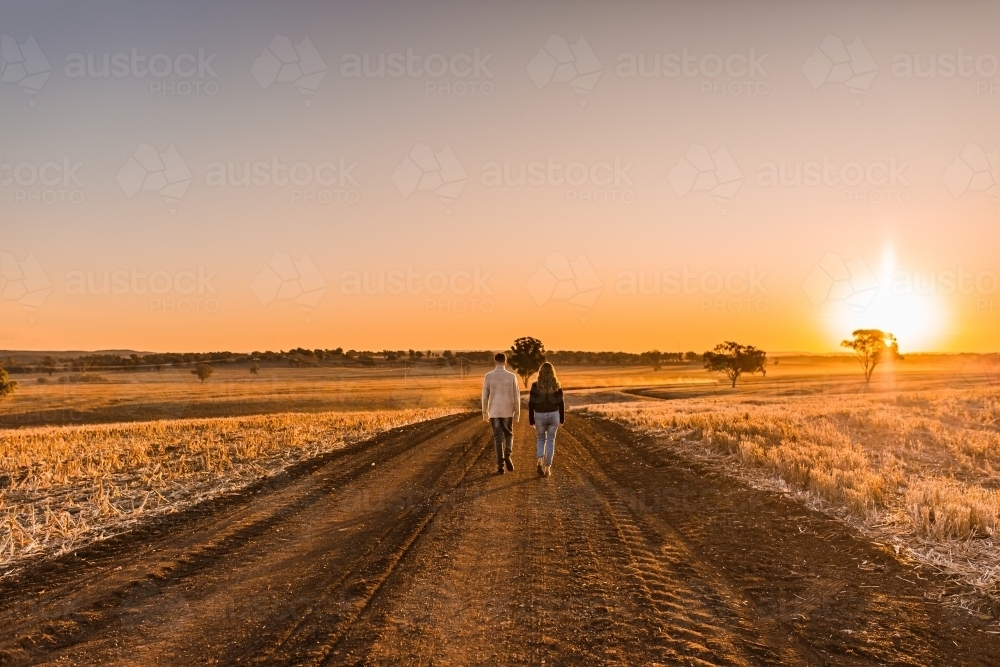 Boy and girl walking together on rural dirt road at sunset - Australian Stock Image