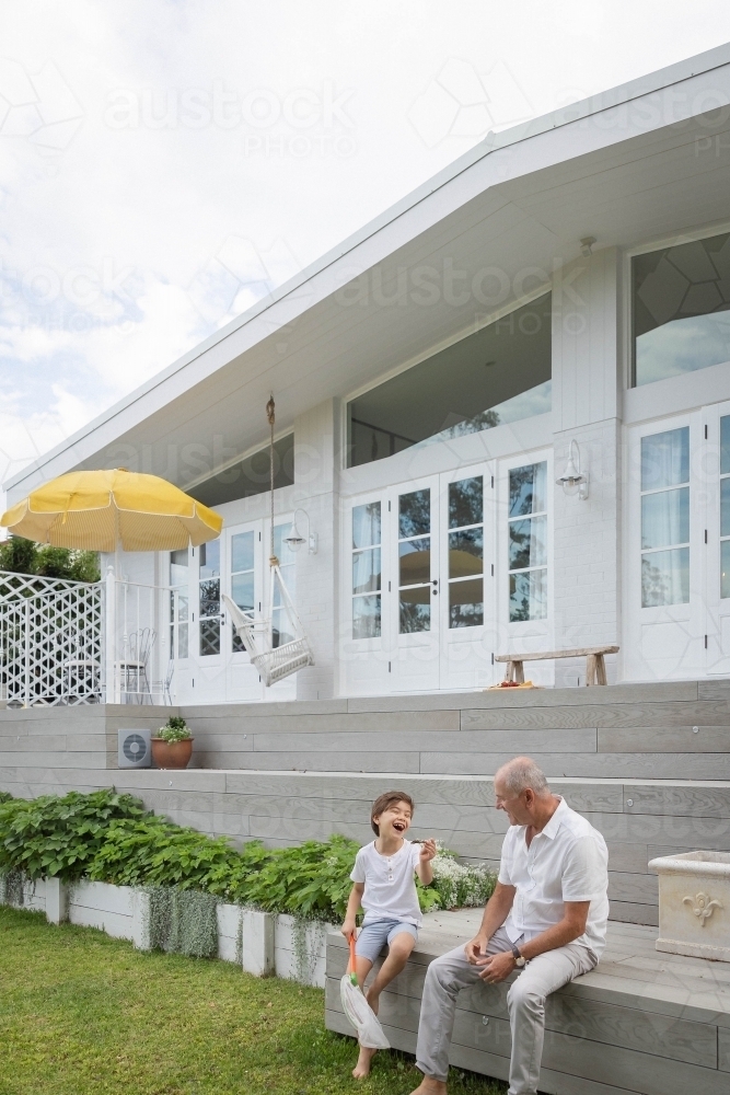 Boy and grandfather sitting together in backyard - Australian Stock Image
