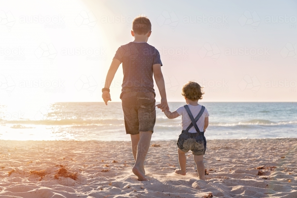 Boy And Little Girl Walking Towards The Ocean At Golden Sunset - Australian Stock Image