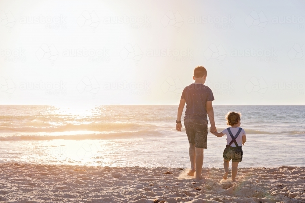 Boy And Little Girl Walking Towards The Ocean At Sunset - Australian Stock Image