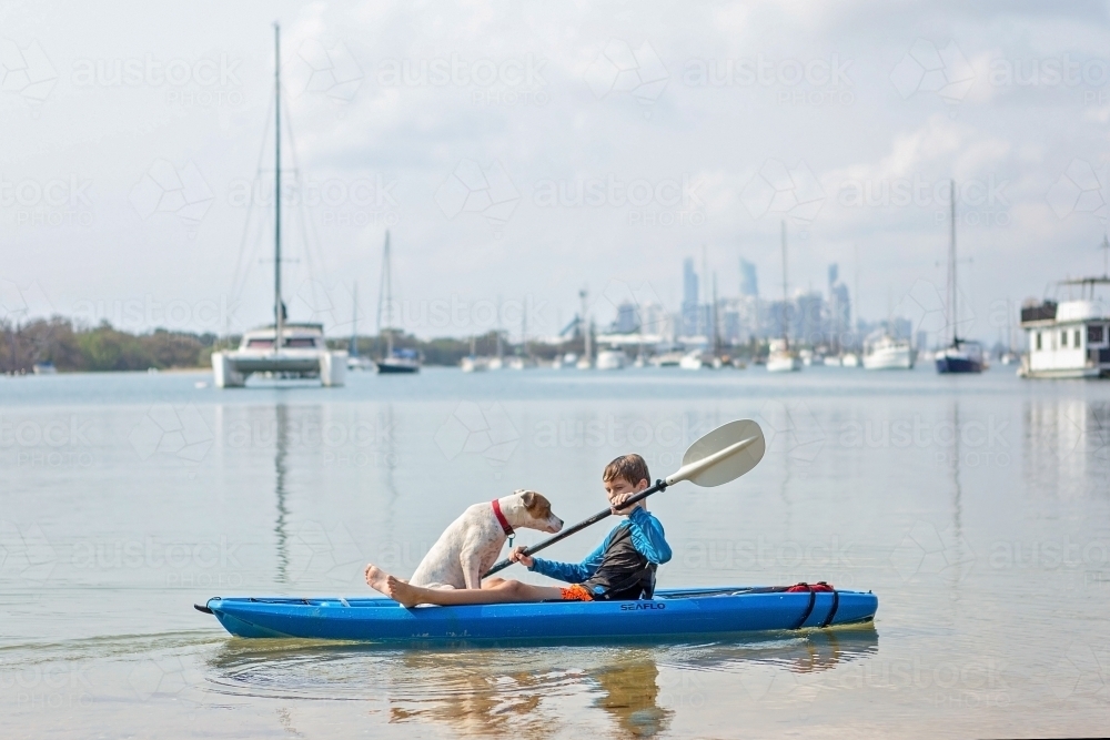 Boy at play with dog on kayak in water - Australian Stock Image