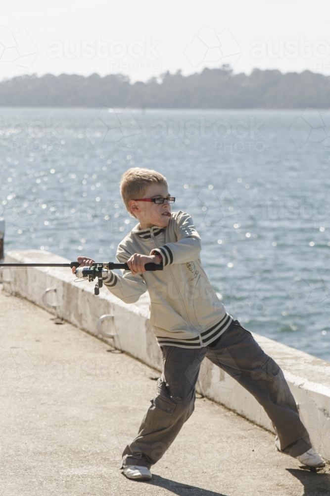 Boy casting line to go fishing off wharf on sunny day - Australian Stock Image