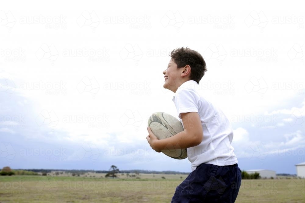 Boy catching a football in a rural paddock - Australian Stock Image