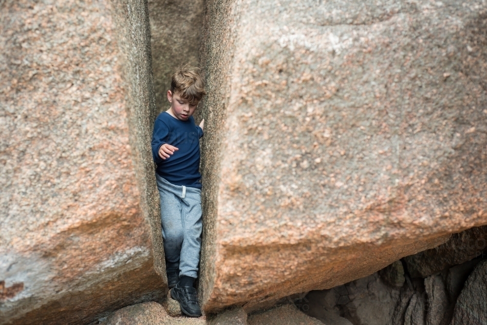 Boy climbing through two boulder rocks - Australian Stock Image